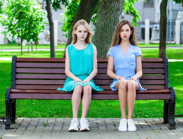 Δύο Νεαρά Κορίτσια Καλοκαιρινά Φορέματα Κάθονται Ένα Παγκάκι Στο Πάρκο — Φωτογραφία Αρχείου