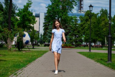 Yazlık parkta poz veren mavi elbiseli güzel esmer bir kızın portresi.