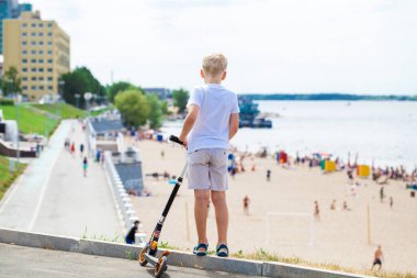 Şehir parkında scooter süren küçük bir çocuk.