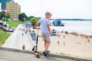 Şehir parkında scooter süren küçük bir çocuk.