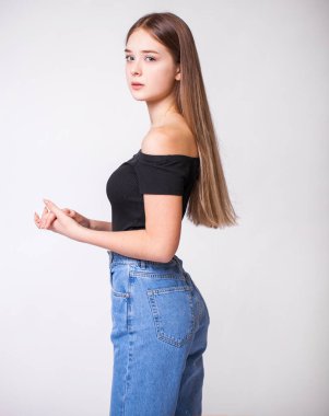 Kot pantolonlu güzel, seksi esmer kadın. Kot pantolon giymiş bir manken. Gri stüdyo arka planında izole edilmiş.