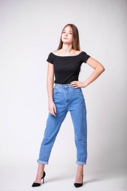 Kot pantolonlu güzel, seksi esmer kadın. Kot pantolon giymiş bir manken. Gri stüdyo arka planında izole edilmiş.