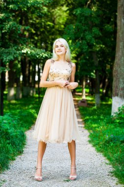 Açık hava parkında bej elbiseli güzel bir sarışının vücut portresi.