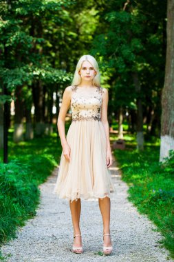 Açık hava parkında bej elbiseli güzel bir sarışının vücut portresi.