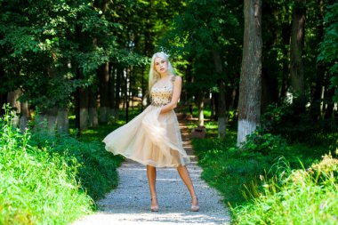 Açık hava parkında bej elbiseli güzel bir sarışının vücut portresi.