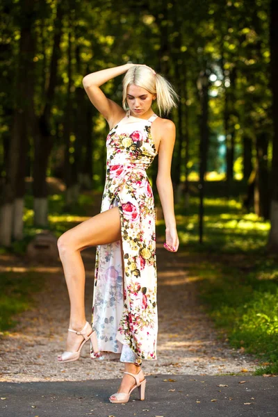 Uzun çiçekli bir elbise giymiş sarışın bir kadının tüm vücut portresi.