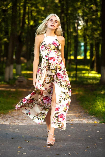 Uzun çiçekli bir elbise giymiş sarışın bir kadının tüm vücut portresi.