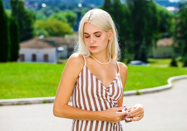 Çizgili bir yaz elbisesi içinde, güneşli bir havada sokakta poz veren genç, güzel bir sarışın.