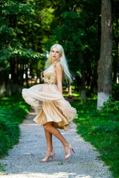 Açık hava parkında bej elbiseli güzel bir sarışının vücut portresi.