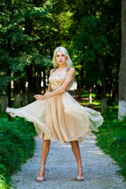 Açık hava parkında bej elbiseli güzel bir sarışının vücut portresi.