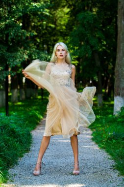 Açık hava parkında bej elbiseli güzel bir sarışının vücut portresi.