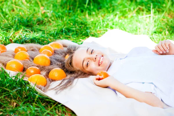 年轻的少女躺在草坪上的毛毯上 头发上长着橘子 — 图库照片