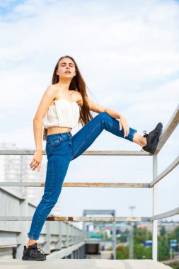 Beyaz bluzlu, mavi kotlu güzel esmer bir mankenin portresi.