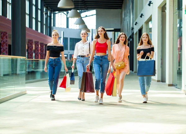 Alışveriş merkezinde beş genç kız arkadaş ellerinde çantalarla dolaşıyorlar.