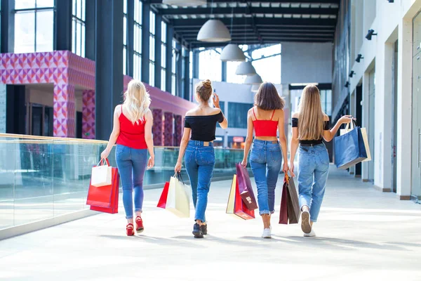 Kadın alışverişi. Arkaya bakan genç kızlar alışveriş merkezinde çantalarla yürüyorlar.