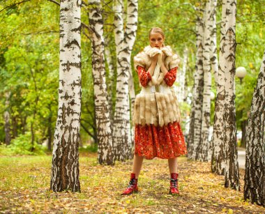 Rus güzellik kadını. Sonbahar ormanlarında poz veren uzun kırmızı çiçekli bir modelin vücut portresi.