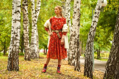 Rus güzellik kadını. Sonbahar ormanlarında poz veren uzun kırmızı çiçekli bir modelin vücut portresi.