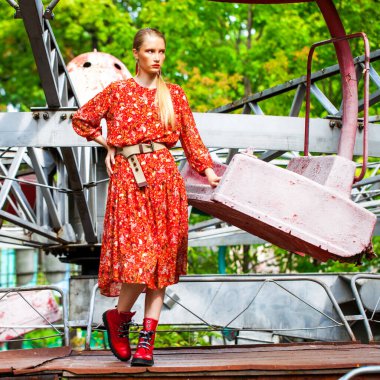 Uzun kırmızı çiçekli şık bir modelin tüm vücut portresi eğlence parkının arka planında poz veriyor. 