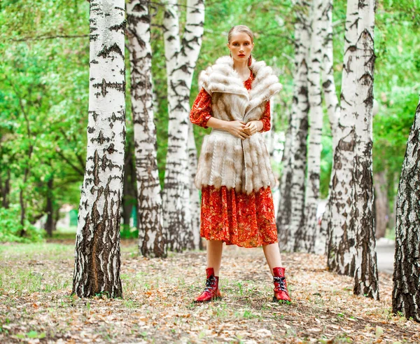 ロシアの美人 秋の森の中でポーズをとる長い赤い花のドレスと毛皮のベストのスタイリッシュなモデルの全身肖像画 — ストック写真