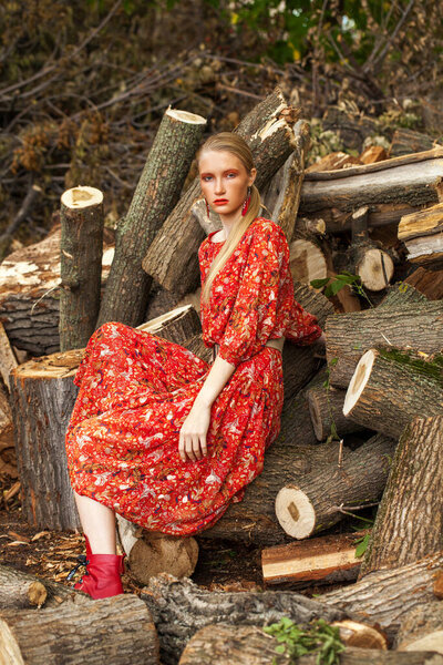 Fashion model portrait. Young beautiful blonde woman posing against the background of sawn logs in the forest