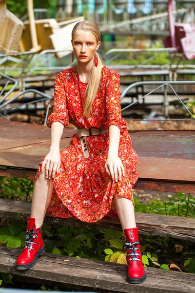 遊園地を背景にポーズをとった長い赤い花のドレスのスタイリッシュなモデルの全身肖像画 — ストック写真