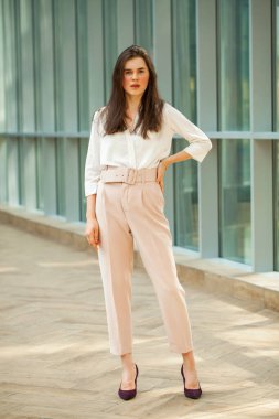 Tam boy portre, beyaz bluz ve ofiste pembe pantolon giyen güzel esmer kadın.