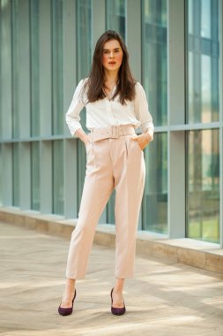 Tam boy portre, beyaz bluz ve ofiste pembe pantolon giyen güzel esmer kadın.