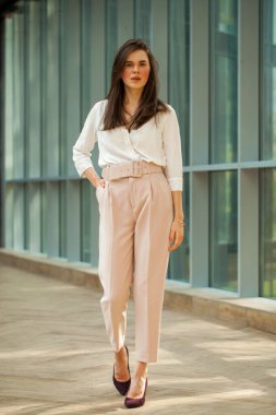 Tam boy portre, beyaz bluz ve ofiste pembe pantolon giyen güzel esmer kadın.