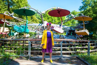 Sarı ceketli şık bir mankenin portresi lunaparkın arka planında poz veriyor. 