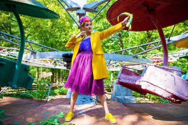 Sarı ceketli şık bir mankenin portresi lunaparkın arka planında poz veriyor. 