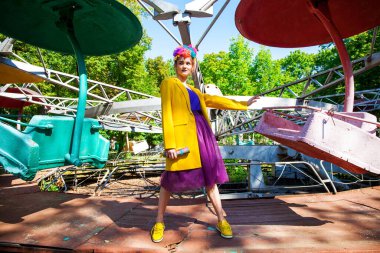 Sarı ceketli şık bir mankenin portresi lunaparkın arka planında poz veriyor. 