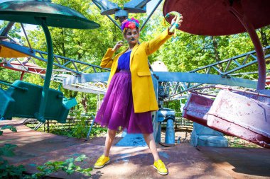 Sarı ceketli şık bir mankenin portresi lunaparkın arka planında poz veriyor. 