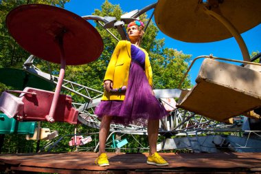 Sarı ceketli şık bir mankenin portresi lunaparkın arka planında poz veriyor. 