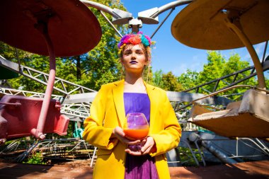 Sarı ceketli şık bir mankenin portresi lunaparkın arka planında poz veriyor. 