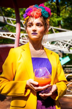 Sarı ceketli şık bir mankenin portresi lunaparkın arka planında poz veriyor. 