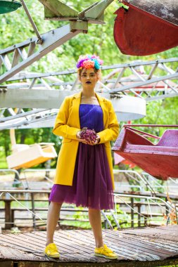 Sarı ceketli şık bir mankenin portresi lunaparkın arka planında poz veriyor. 