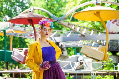 Güzel elbiseli genç bir kız eğlence parkının arka planında poz veriyor.