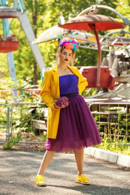 Güzel elbiseli genç bir kız eğlence parkının arka planında poz veriyor.