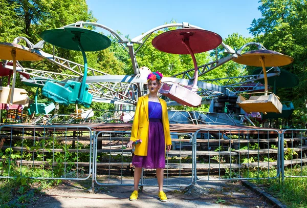 Sarı ceketli şık bir mankenin portresi lunaparkın arka planında poz veriyor. 