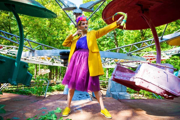 Sarı ceketli şık bir mankenin portresi lunaparkın arka planında poz veriyor. 