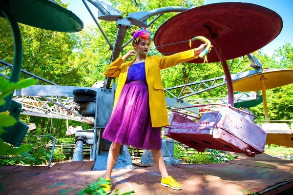 Sarı ceketli şık bir mankenin portresi lunaparkın arka planında poz veriyor. 