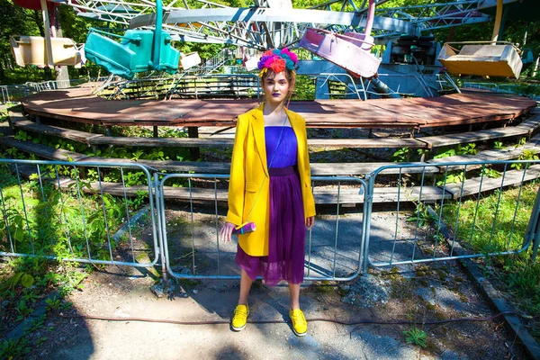 Sarı ceketli şık bir mankenin portresi lunaparkın arka planında poz veriyor. 