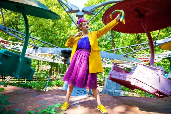 Sarı ceketli şık bir mankenin portresi lunaparkın arka planında poz veriyor. 