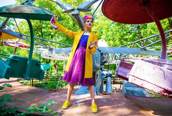 Sarı ceketli şık bir mankenin portresi lunaparkın arka planında poz veriyor. 