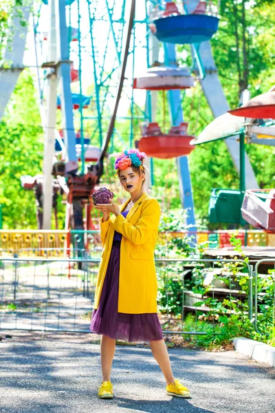 Sarı ceketli şık bir mankenin portresi lunaparkın arka planında poz veriyor. 