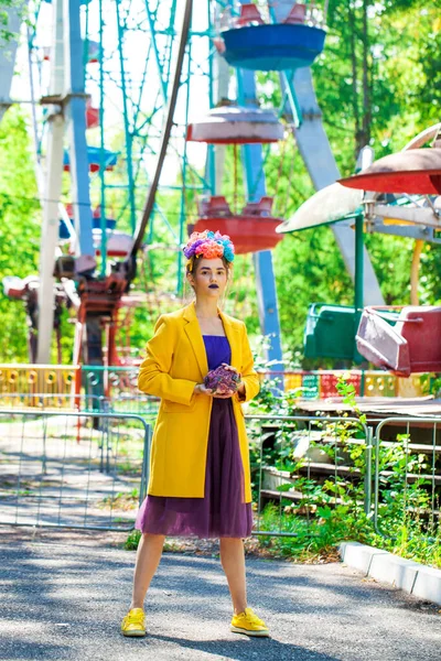 Sarı ceketli şık bir mankenin portresi lunaparkın arka planında poz veriyor. 