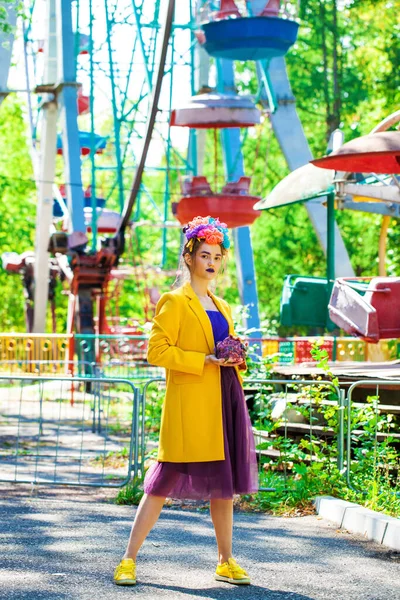 Sarı ceketli şık bir mankenin portresi lunaparkın arka planında poz veriyor. 