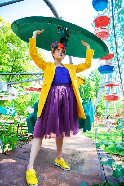 Sarı ceketli şık bir mankenin portresi lunaparkın arka planında poz veriyor. 