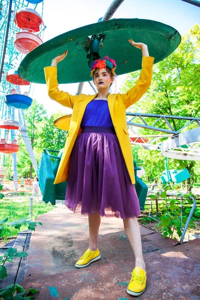 Sarı ceketli şık bir mankenin portresi lunaparkın arka planında poz veriyor. 