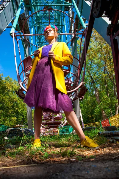 Sarı ceketli şık bir mankenin portresi lunaparkın arka planında poz veriyor. 